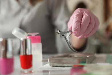 Professional manicurist with nippers at table in beauty salon, closeup