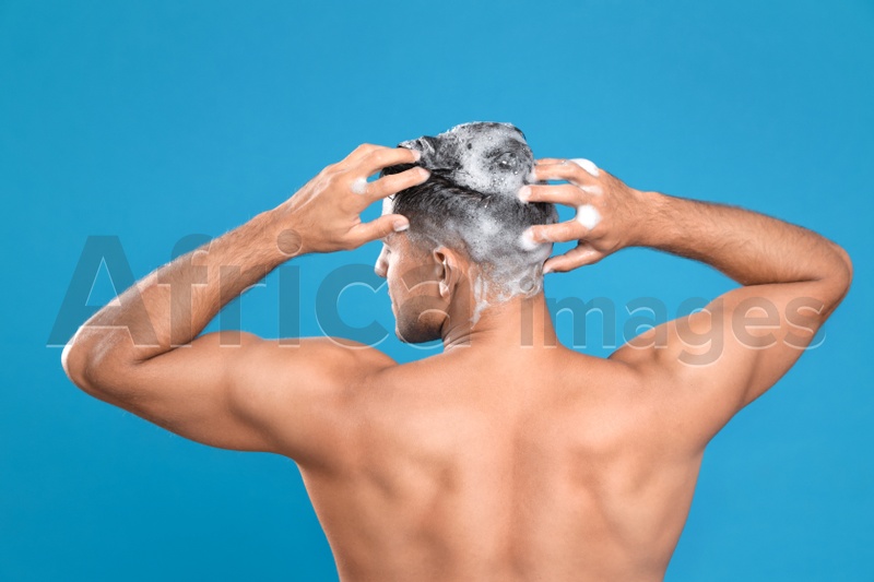 Handsome man washing hair on light blue background, back view