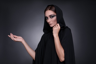 Mysterious witch in mantle with hood on dark background