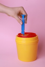 Woman throwing used syringe into sharps container  on pink background, closeup