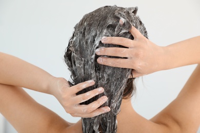 Woman applying shampoo onto her hair against light background