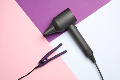 Hair dryer and iron on color background, flat lay. Professional hairdresser tool
