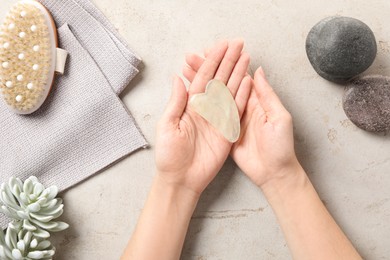 Photo of Woman holding gua sha tool over light stone table, top view