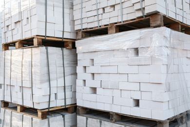Photo of Pallets with white bricks outdoors. Building materials wholesale
