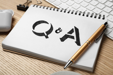 Notebook with text Q&A and pen on wooden table, closeup