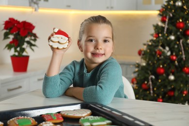 Cute little girl with freshly baked Christmas gingerbread cookie at table indoors