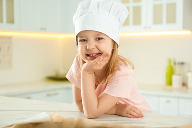 Portrait of cute little girl wearing chef hat in kitchen