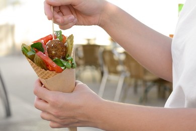 Woman eating wafer with falafel and vegetables outdoors, closeup. Street food