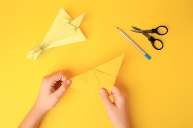 Photo of Origami art. Child holding paper figure on yellow background, closeup and top view