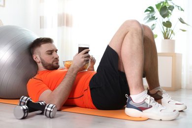 Lazy young man eating junk food on yoga mat at home