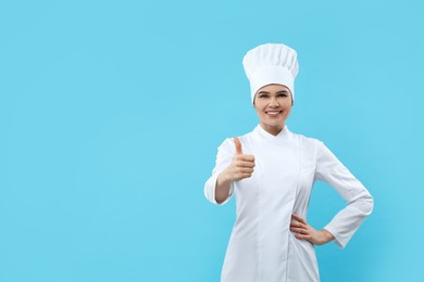 Photo of Happy female chef showing thumbs up on light blue background. Space for text