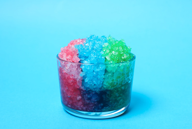 Rainbow shaving ice in glass dessert bowl on light blue background, closeup