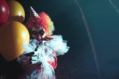 Terrifying clown with air balloons outdoors at night. Halloween party costume