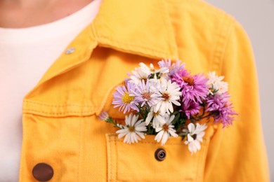 Woman with beautiful tender flowers in jacket's pocket on light background, closeup