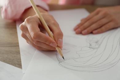 Woman drawing girl's portrait with pencil on sheet of paper at wooden table, closeup