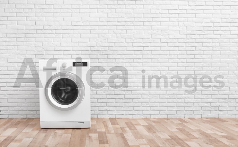 Photo of Modern washing machine near brick wall in empty laundry room, space for text