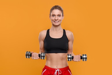 Photo of Portrait of sportswoman exercising with dumbbells on yellow background