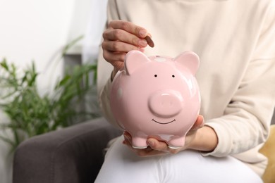 Woman putting coin into piggy bank at home, closeup