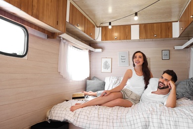 Happy young couple on bed in trailer, space for text. Camping vacation