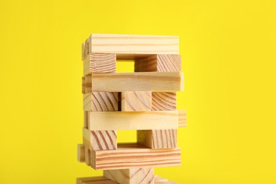 Jenga tower made of wooden blocks on yellow background, closeup