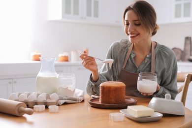 Young woman decorating traditional Easter cake with glaze in kitchen