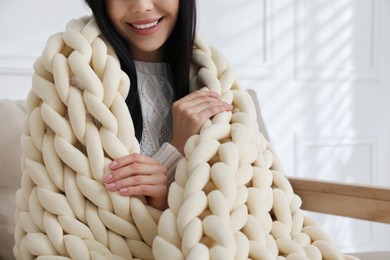 Photo of Woman with chunky knit blanket on sofa at home, closeup