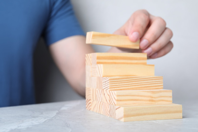 Photo of Man building steps with wooden blocks on light grey marble table, closeup. Career ladder