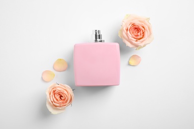Bottle of perfume, beautiful roses and petals on white background, flat lay