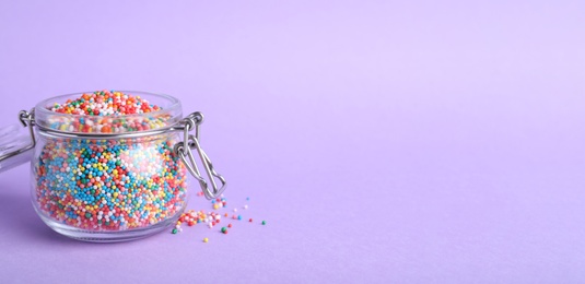 Colorful sprinkles in jar on lilac background, space for text. Confectionery decor
