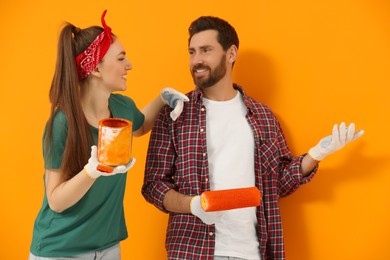 Photo of Happy designers with painting equipment near freshly painted orange wall