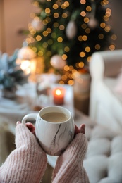 Woman with cup of cocoa in room decorated for Christmas, closeup