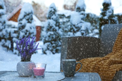 Photo of Burning candle, potted flowers and cup of hot drink on coffee table outdoors. Cosy winter