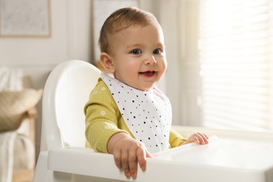 Cute little baby wearing bib in highchair at home