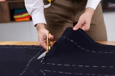 Photo of Dressmaker cutting fabric by following chalked sewing pattern in workshop, closeup