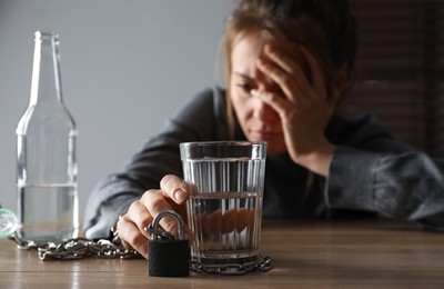 Alcohol addiction. Woman chained with glass of vodka at wooden table in room, focus on hand