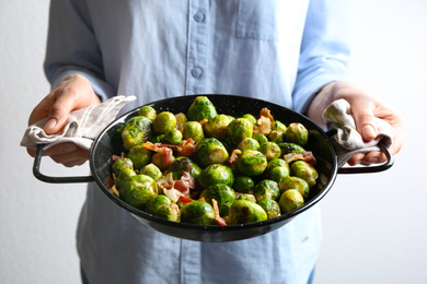 Woman holding wok with Brussels and bacon on light background, closeup