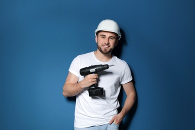 Young working man with electric screwdriver on color background