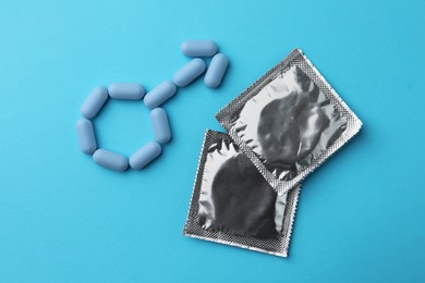 Photo of Male sign made of pills and condoms on light blue background, flat lay. Potency problem
