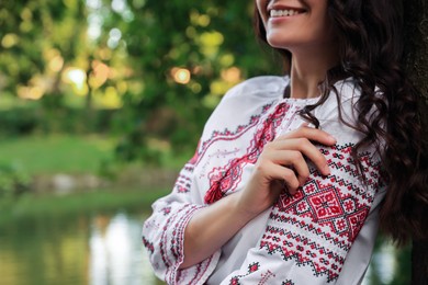 Photo of Woman in beautiful embroidered shirt near lake, closeup with space for text. Ukrainian national clothes