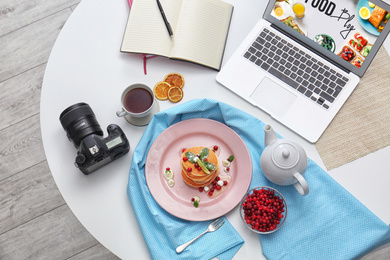Flat lay composition with delicious pancakes, camera and laptop on white table. Food blog