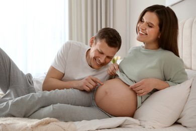 Photo of Young pregnant woman with her husband in bedroom