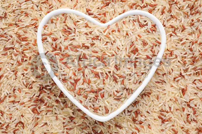 Mix of brown and polished rice with heart shaped bowl, top view
