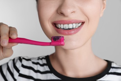 Woman brushing teeth with charcoal toothpaste on grey background, closeup