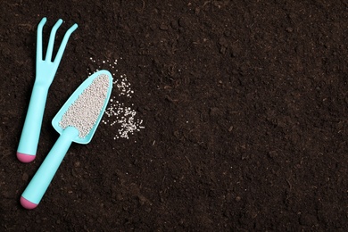Flat lay composition with gardening tools and chemical fertilizer on soil. Space for text