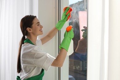 Young woman cleaning window glass with rag and detergent at home