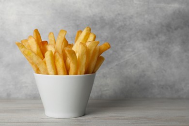Delicious fresh french fries in bowl on light gray wooden table, closeup. Space for text