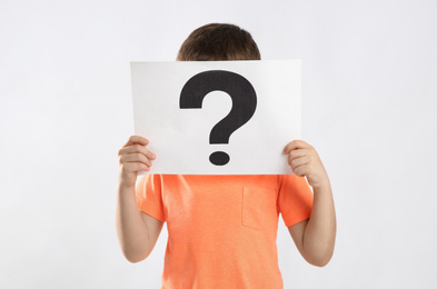 Little boy holding paper with question mark on white background