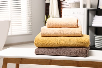 Stack of clean towels on white table in laundry room, space for text