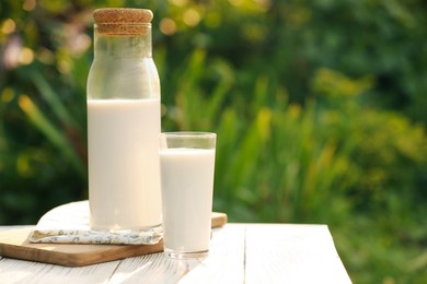 Bottle and glass of tasty fresh milk on white wooden table against blurred background, space for text
