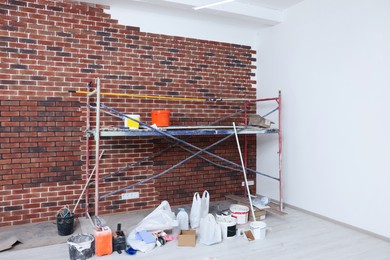 Photo of Scaffolding and equipment near brick wall with tile leveling system in repaired room